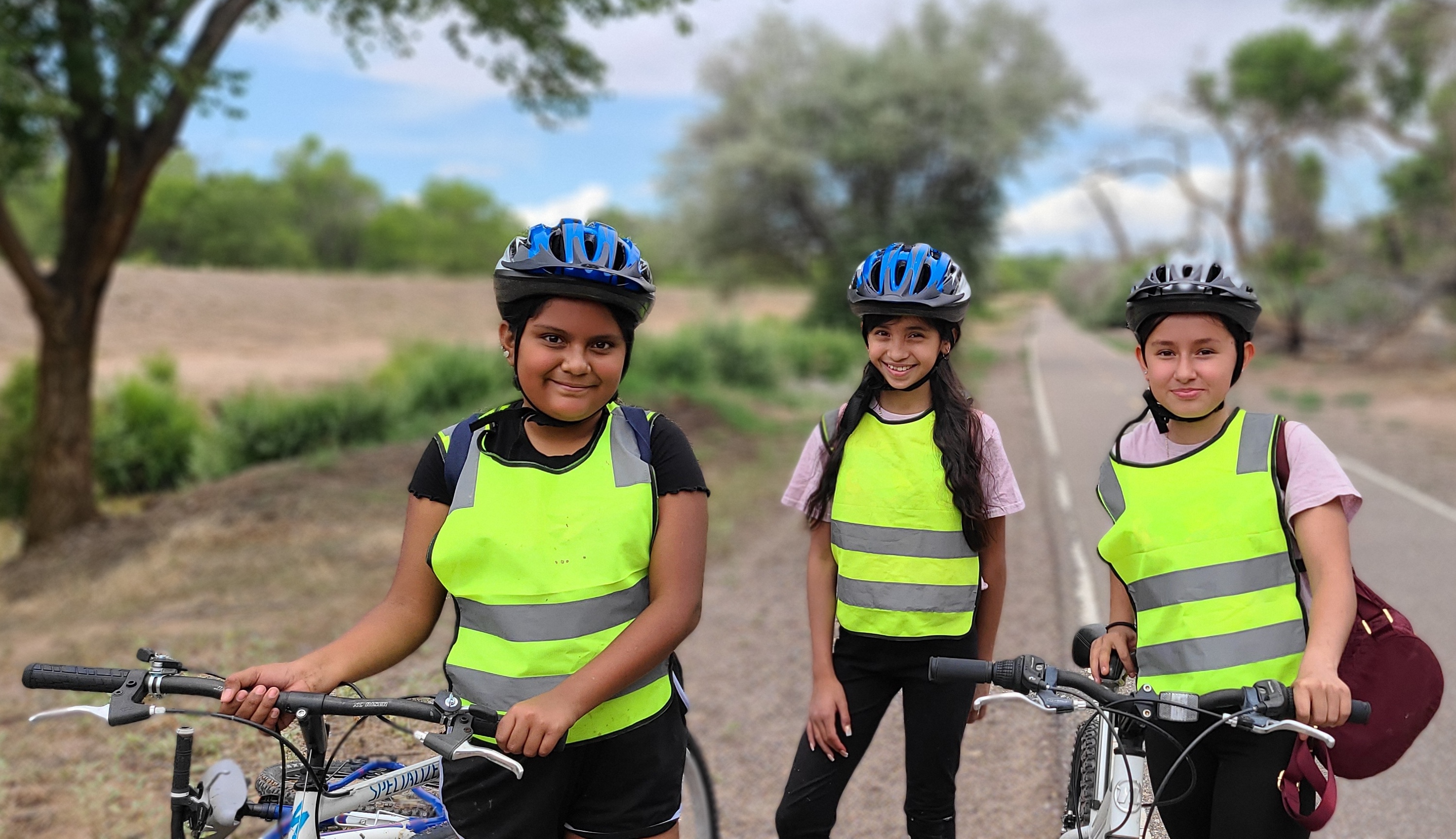 Three young people with bikes and yellow vests look into the camera